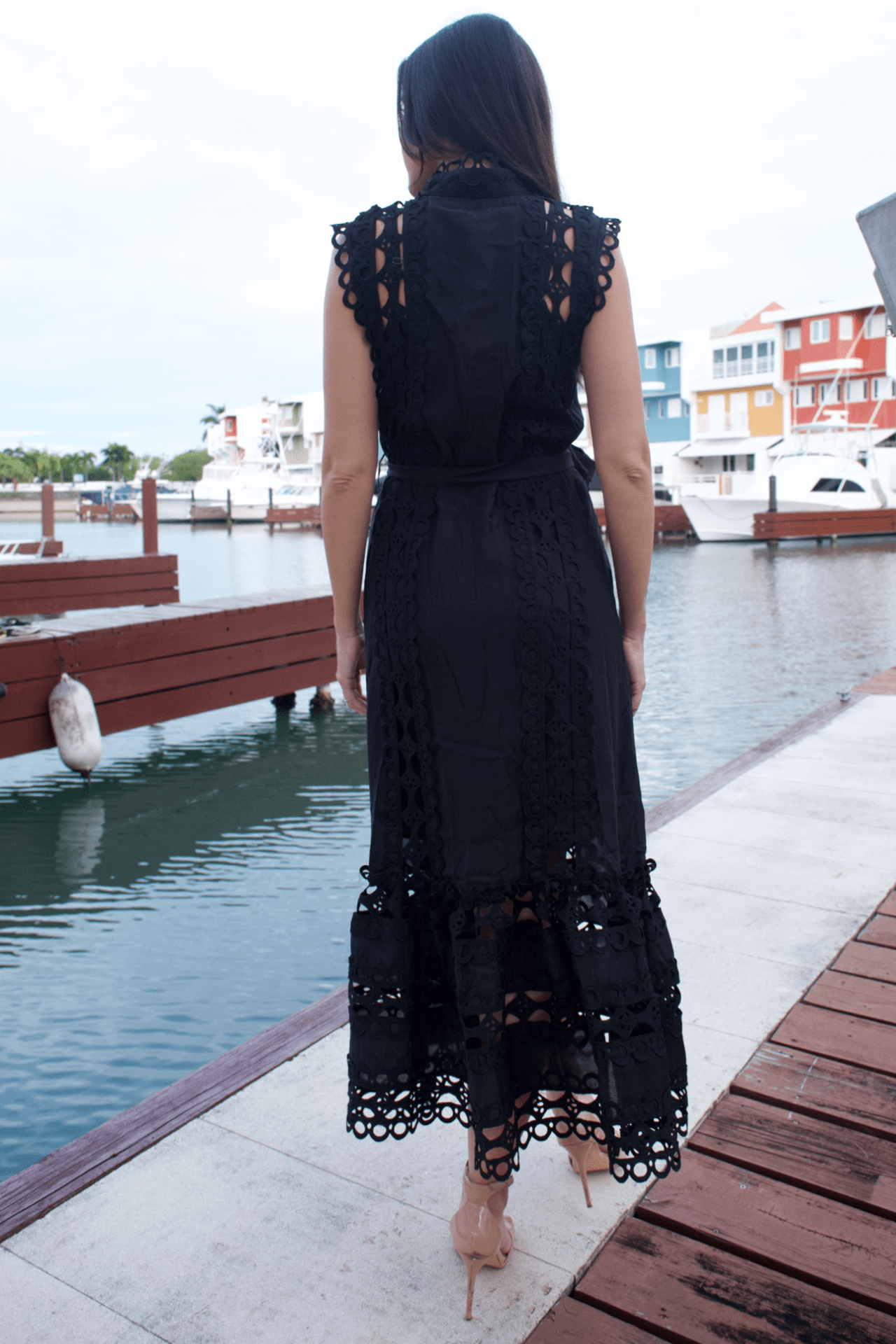 Back view of a women's black maxi lace trim dress with a belt, showcasing the intricate lace accents and flowing silhouette for a sophisticated look.